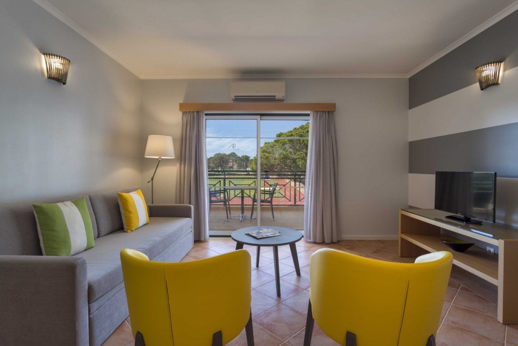 Salon d'appartement avec canapé, deux fauteuils, télévision et balcon surplombant la piste.