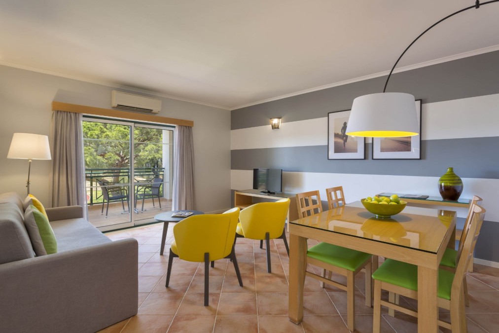 Espace salon et salle à manger d'appartement avec canapé, table et coin balcon.