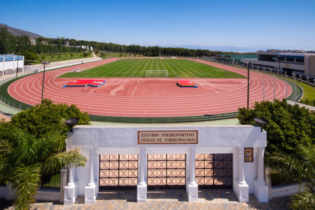 Entrée d'un stade d'athlétisme avec piste de course visible au-delà.