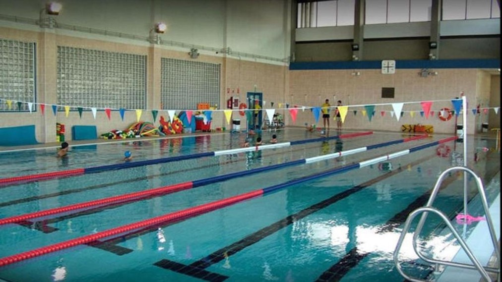 Piscine couverte de 50m avec couloirs marqués, drapeaux de virages et matériel d'entraînement sur le bord du bassin.