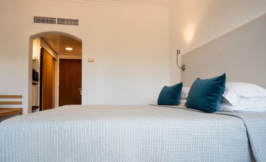 Chambre d'hôtel avec grand lit, linge de lit gris et coussins turquoise au design minimaliste