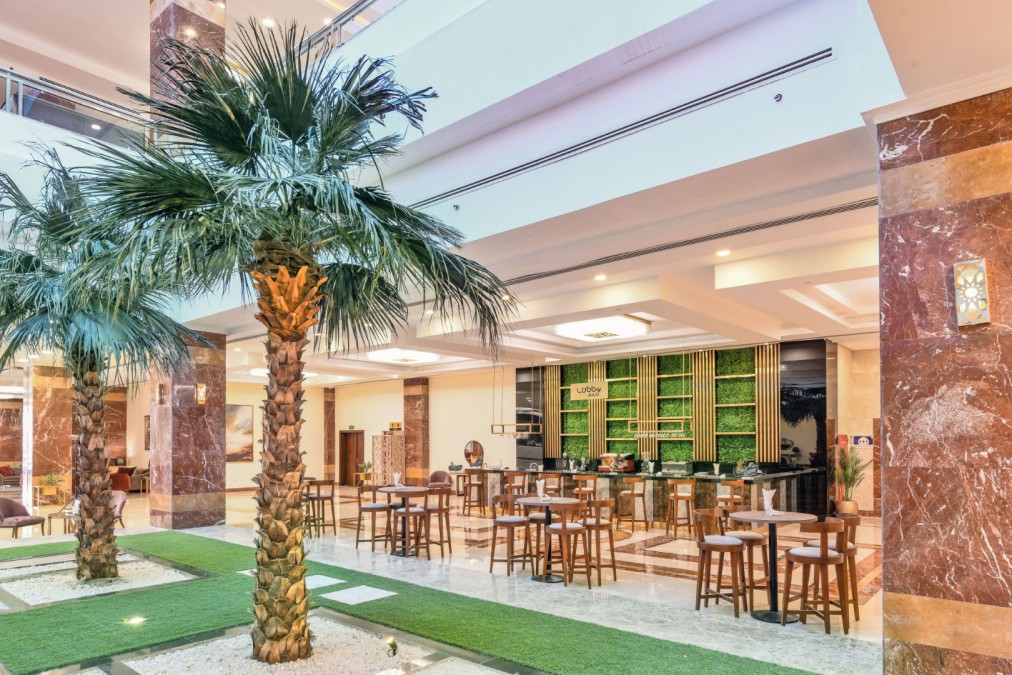 Bar intérieur avec palmiers, tables hautes et étagères vertes