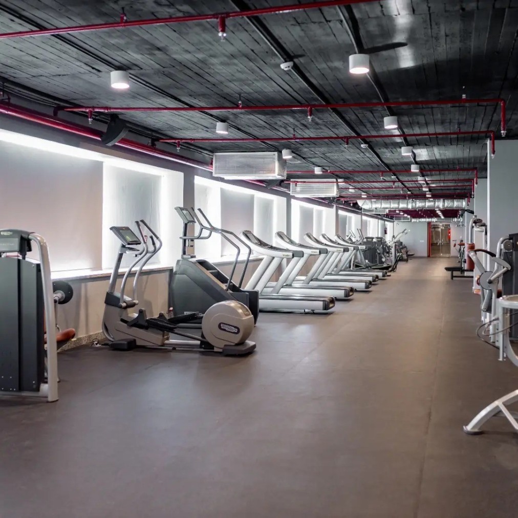 Rangée de tapis de course et vélos elliptiques dans une salle de sport spacieuse avec plafond sombre