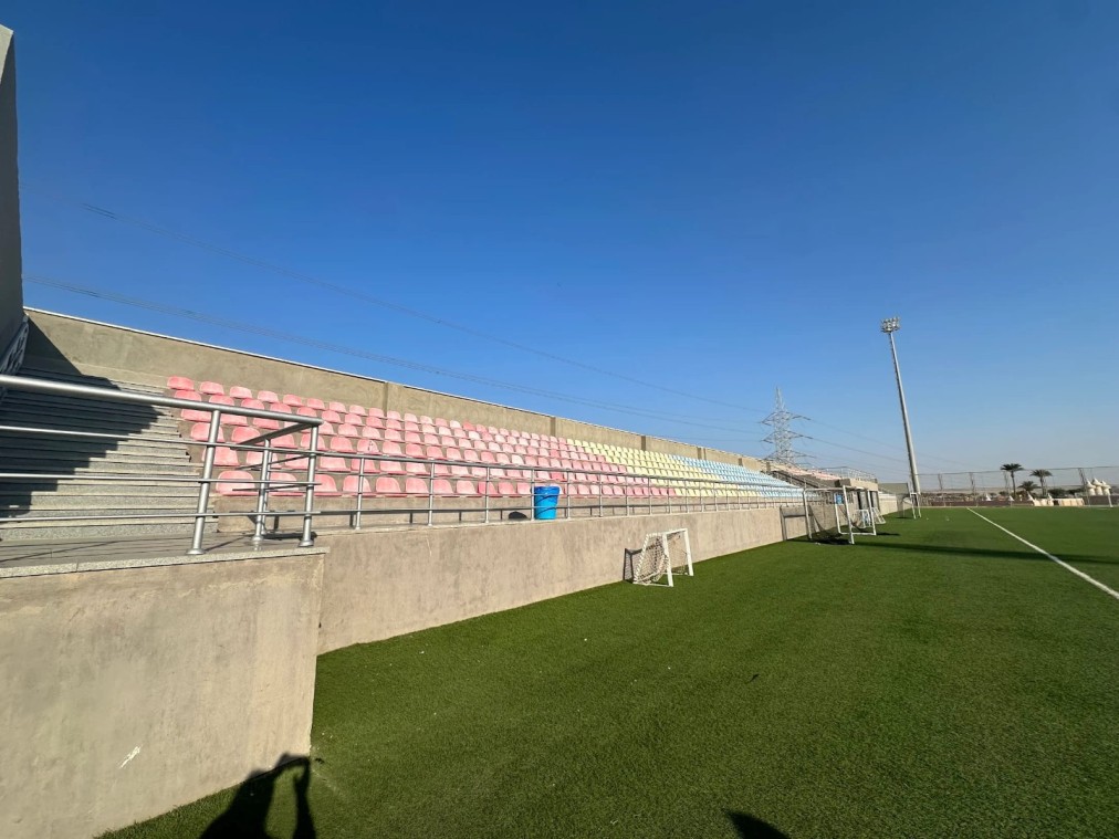 Gradins en béton avec sièges aux couleurs pastel à côté du terrain du centre d'entraînement de football