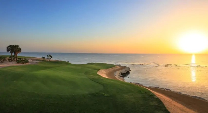 Coucher de soleil sur un fairway côtier et chemin sablonneux au bord de la mer calme.