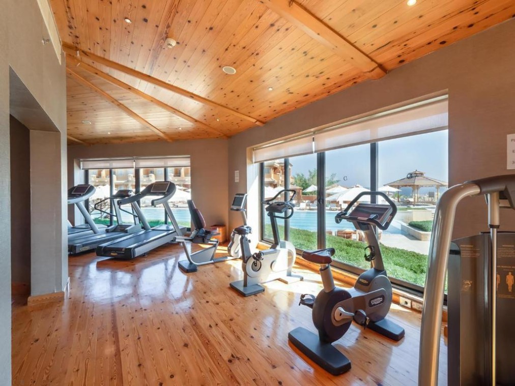 Salle de fitness avec tapis de course et vélos près de grandes fenêtres, espace cardio pour stage d'entraînement