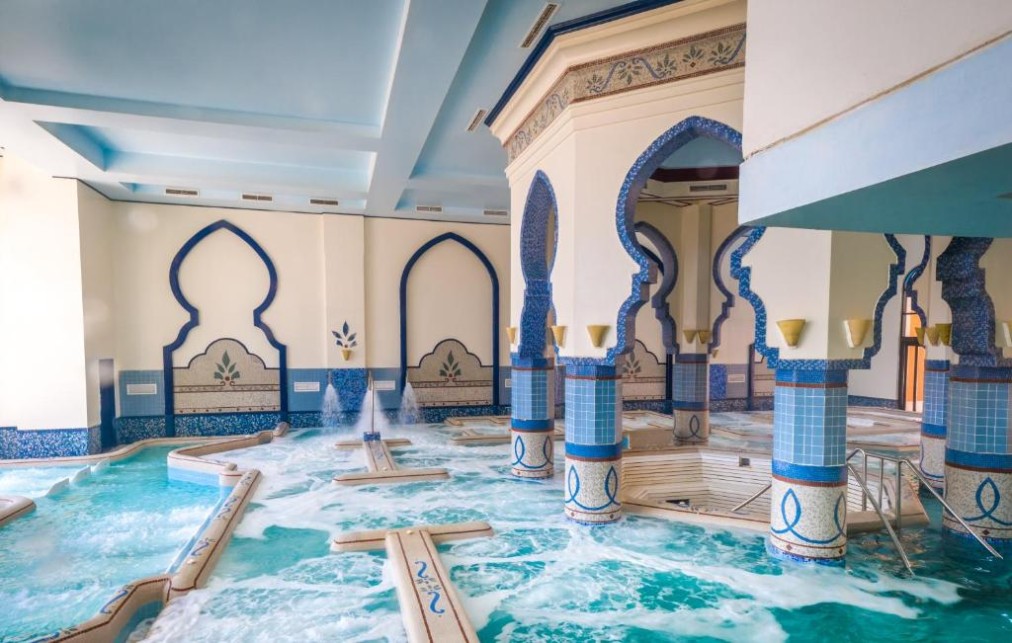 Piscine spa intérieure avec jets d'eau, colonnes en mosaïque bleue et murs voûtés pour récupération après entraînement