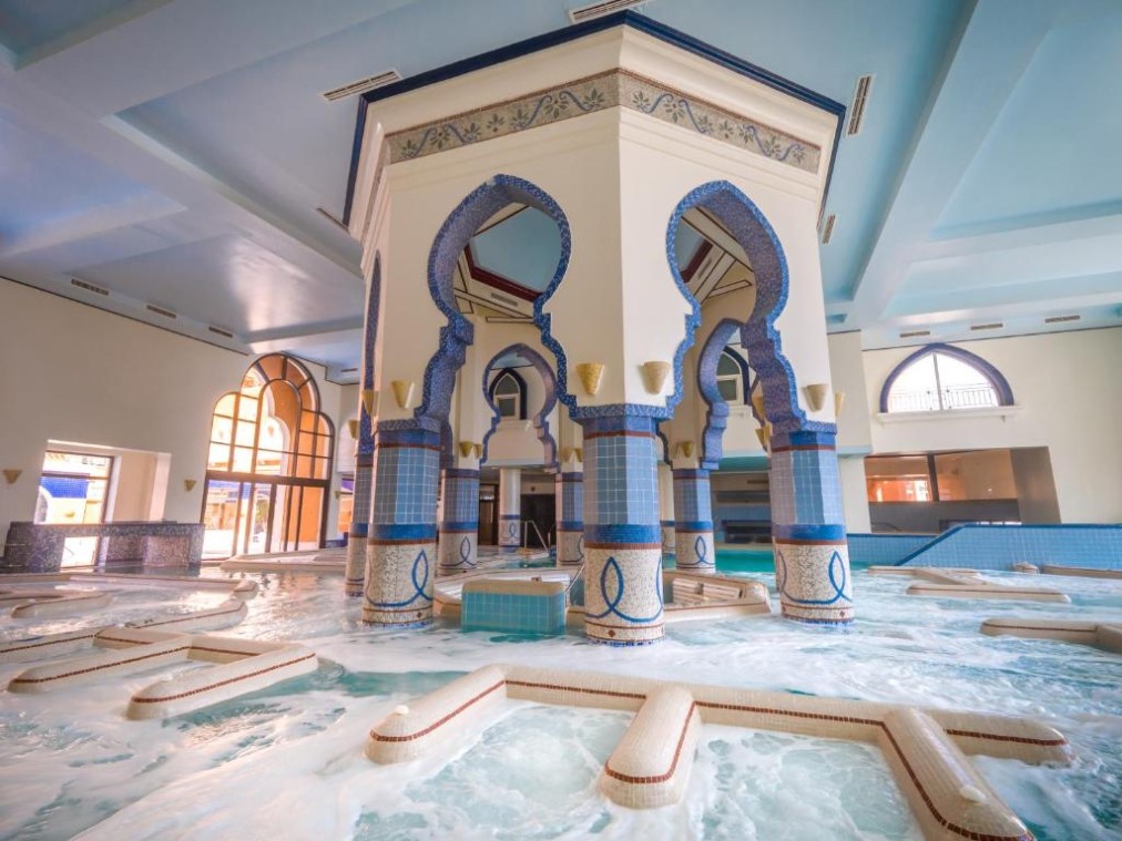 Piscine spa intérieure spacieuse avec colonnes en mosaïque et jeux d'eau pour récupération post-entraînement
