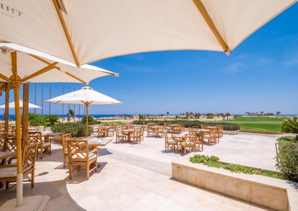 Terrasse extérieure avec parasols surplombant les greens de golf et la mer, idéale pour repas d'équipe