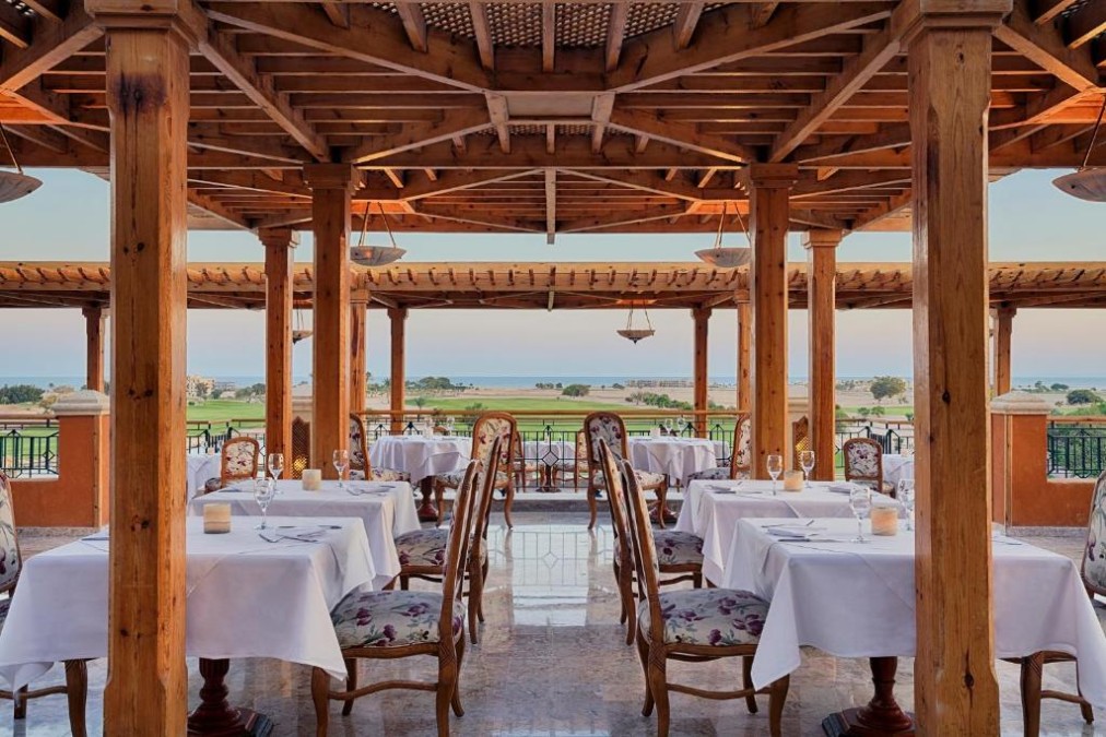 Restaurant sous terrasse couverte avec tables dressées et vues sur le parcours de golf et la mer