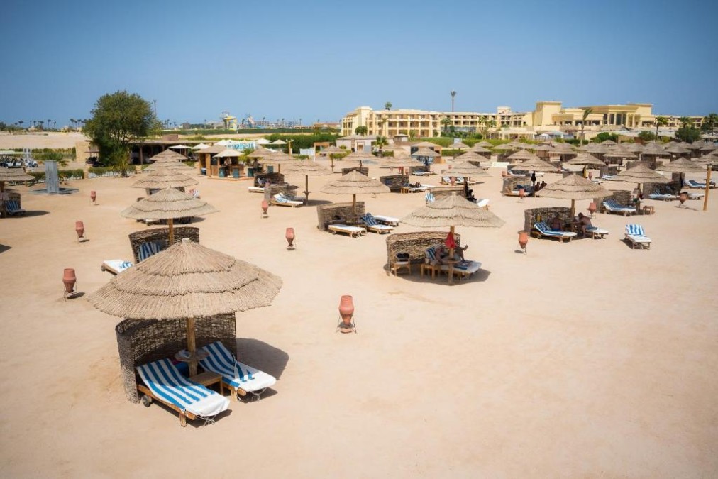 Large plage de sable avec transats et parasols en paille, parfaite pour jours de repos au bord de la mer