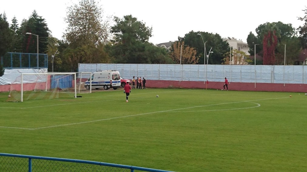 Surface de réparation sur un terrain de football en herbe pendant l'entraînement, avec des plots, des ballons et une ambulance derrière le but.