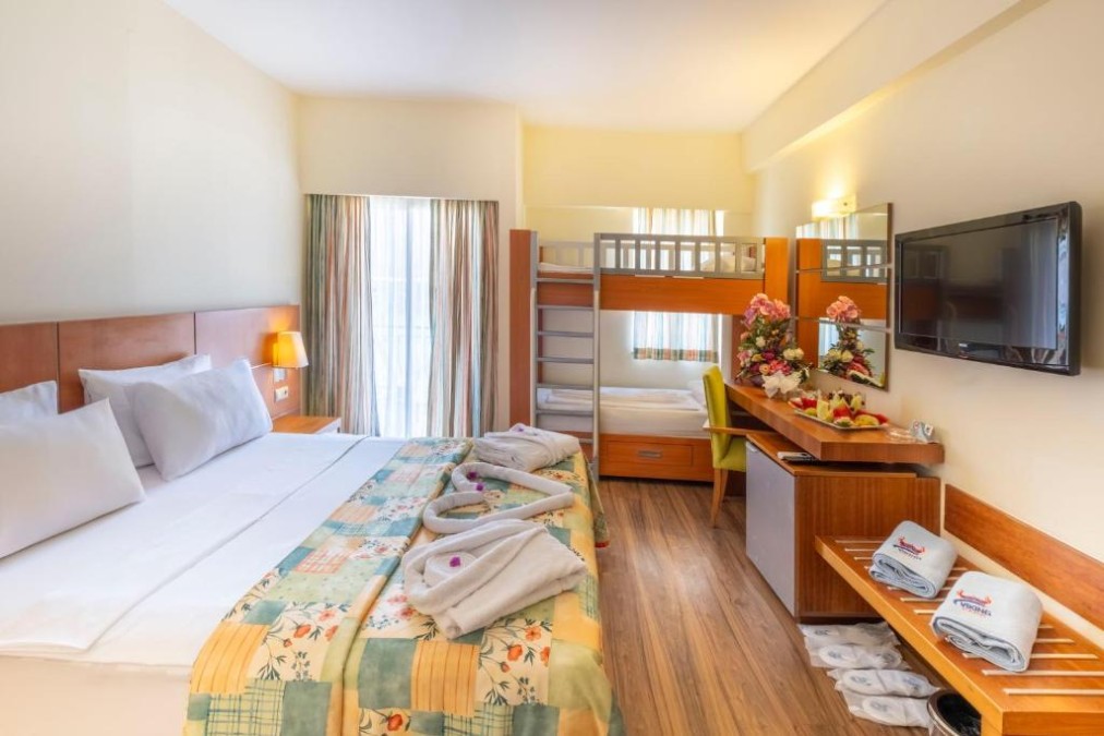 Chambre familiale d'hôtel avec lit double, lits superposés, bureau, TV et rideaux de balcon.