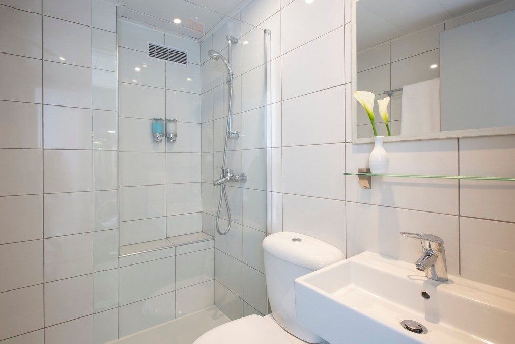 Salle de bain carrelée propre avec douche, toilettes, lavabo et petit vase décoratif