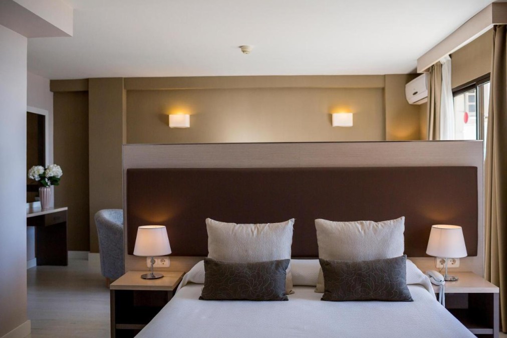 Chambre avec lit double, lampes et mur séparateur menant à un coin salon.