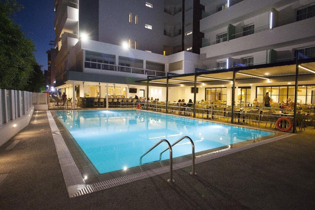 Piscine extérieure de nuit à côté de la terrasse de l'hôtel et du coin bar.
