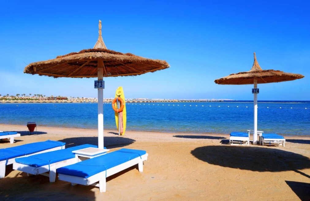 Plage de sable avec transats bleus et parasols en paille face à la mer