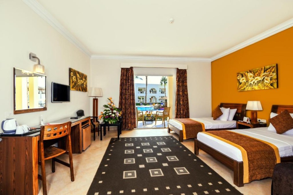 Chambre d'hôtel spacieuse avec lits jumeaux, mobilier en bois et balcon donnant sur la piscine et les palmiers