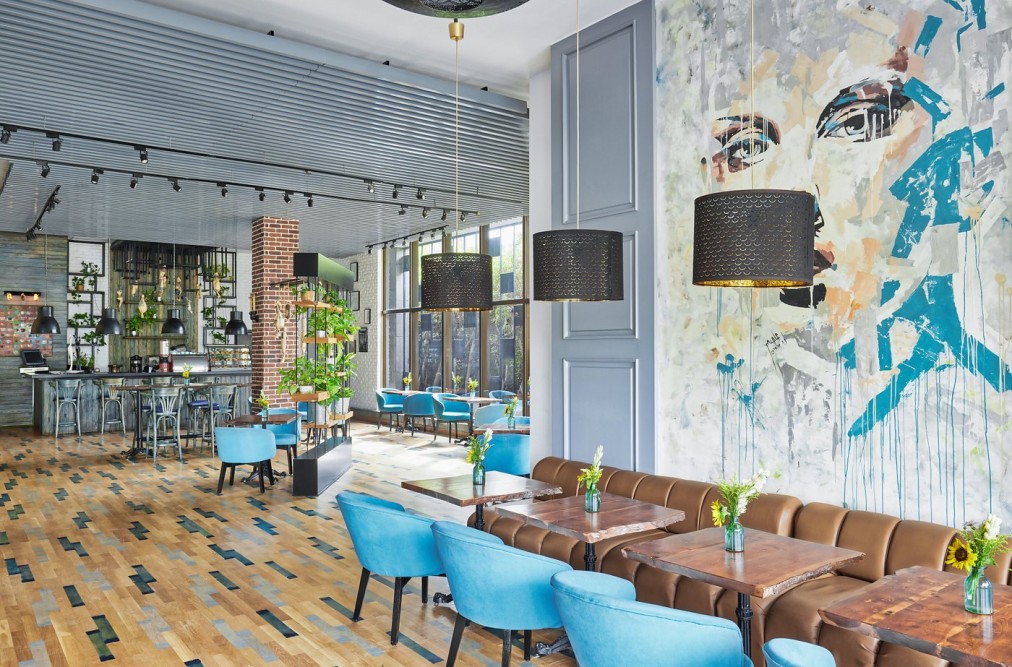 Salon d'hôtel moderne avec fauteuils turquoise, comptoir de bar, suspensions lumineuses et mur à fresque pour temps libre du stage