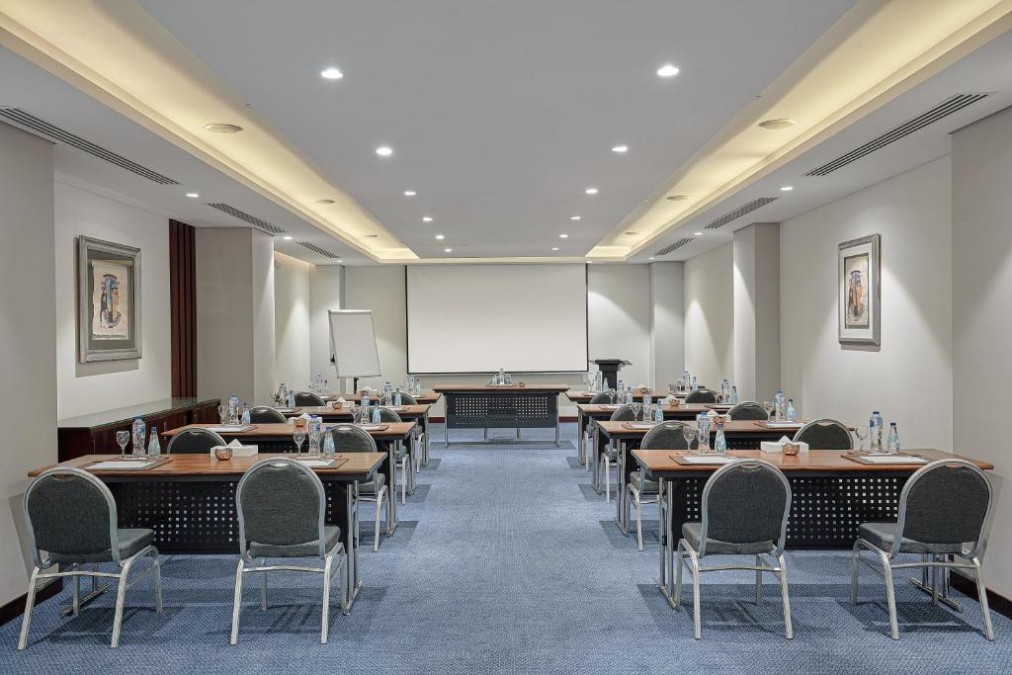 Salle de conférence avec tables en disposition classe, bouteilles d'eau, écran de projection et paperboard pour session de coaching