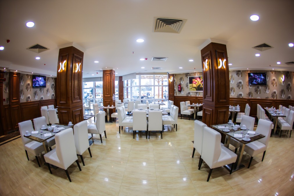 Salle de restaurant avec tables dressées, chaises blanches et colonnes en bois.