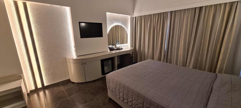 Chambre double avec éclairage d'ambiance, bureau, minibar et rideaux du sol au plafond.