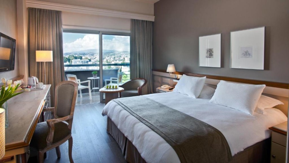 Chambre avec lit double, bureau et balcon donnant sur la ville.