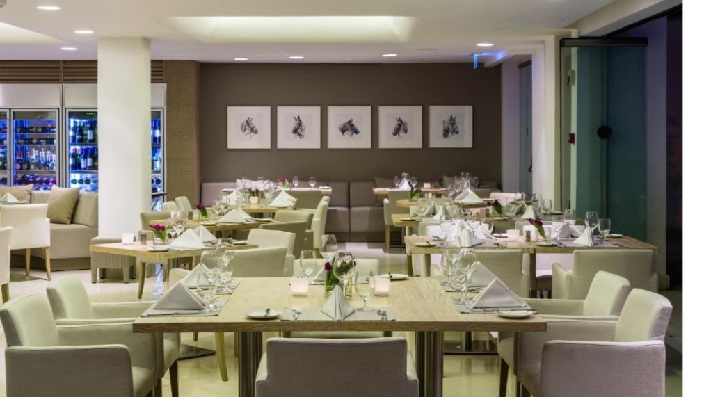 Salle de restaurant avec tables dressées, chaises rembourrées et œuvres d'art encadrées au mur.